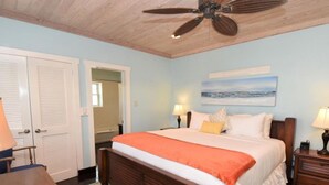 Une chambre à coucher avec un lit, deux tables de chevet avec des lampes, un ventilateur de plafond et un tableau au mur.