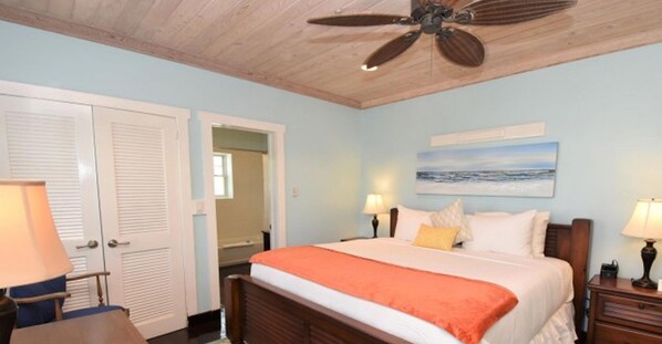 A bedroom with a bed, two bedside tables with lamps, a ceiling fan, and a painting on the wall. - Sapodilla House (Dunmore Town)