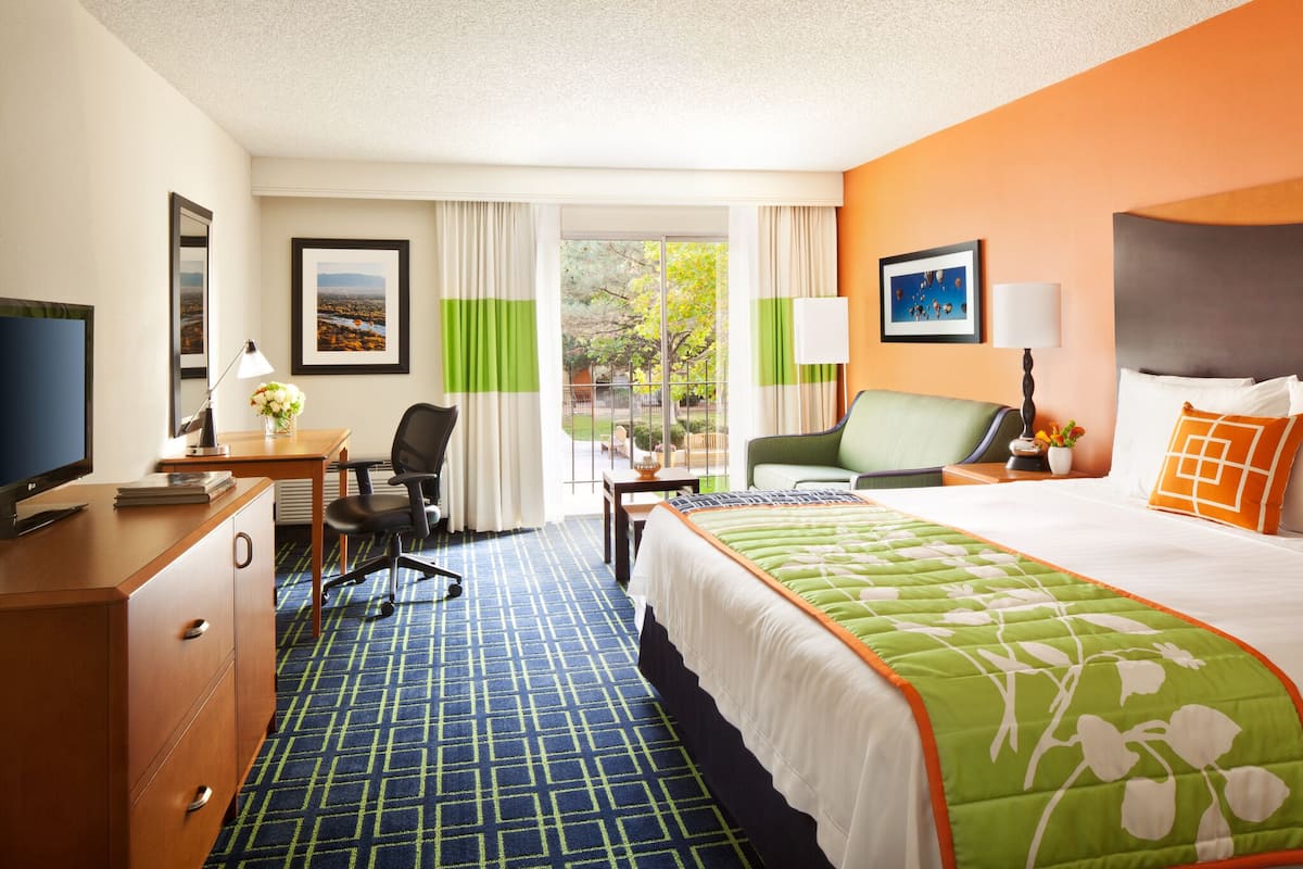 A hotel room with a large bed, a desk with a computer, a chair, a TV, and a window with curtains.