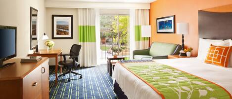 Habitación de hotel con una cama grande, un escritorio con computadora, una silla, televisor y ventana con cortinas.