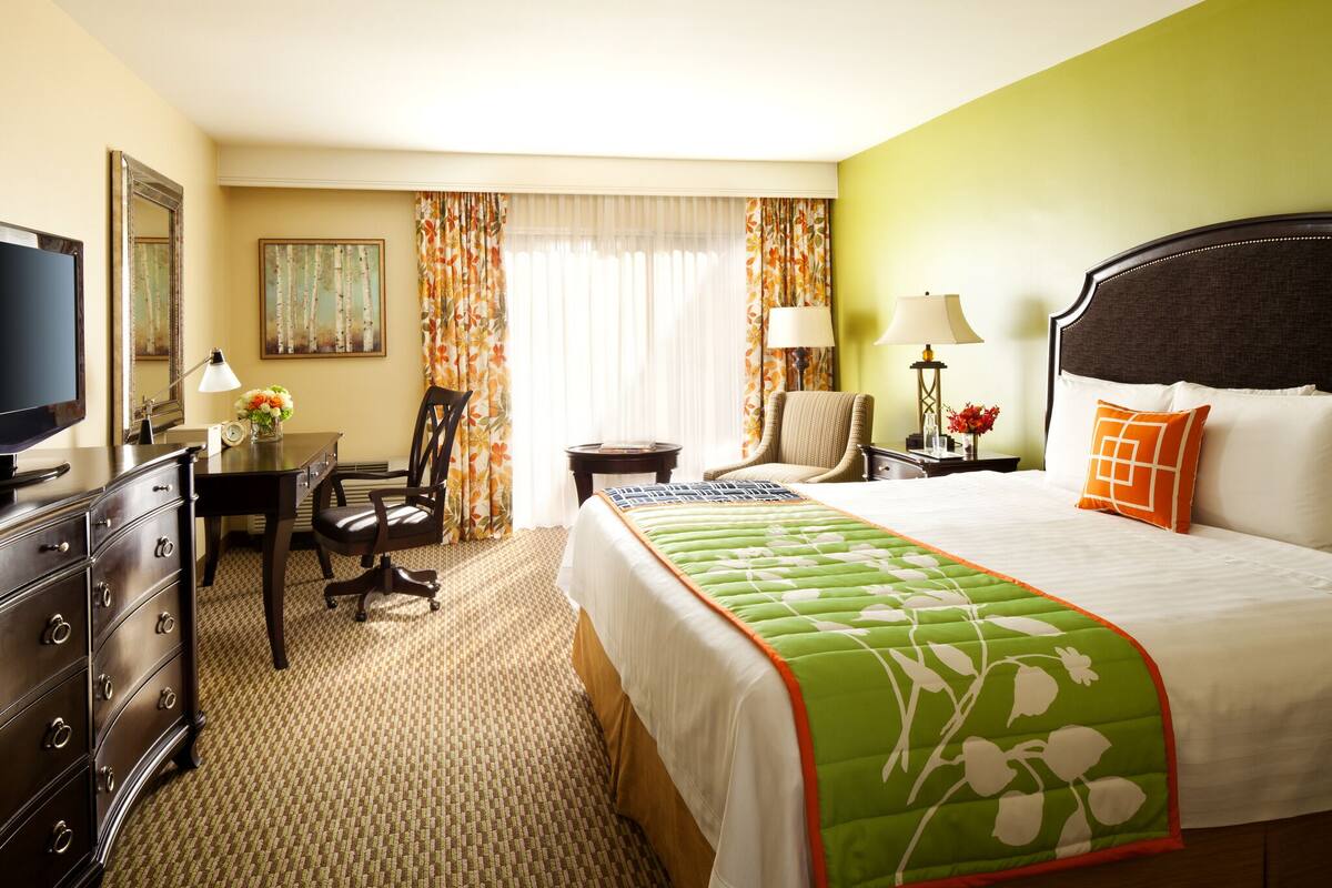 A hotel room with a large bed, a desk, a chair, a television, and a window with curtains.