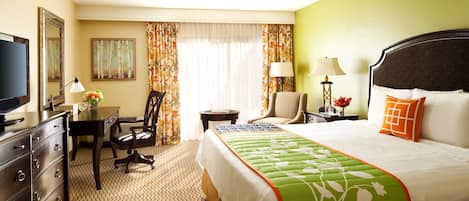 A hotel room with a large bed, a desk, a chair, a television, and a window with curtains.
