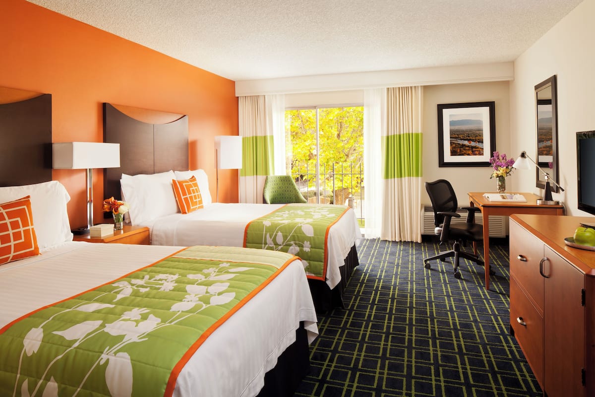 A hotel room with two beds, a desk, a chair, a TV, and a window with curtains.