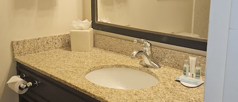 Un baño con lavamanos de granito, espejo y dos toallas colgadas en barras para toallas.