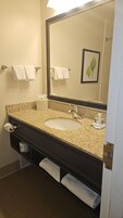 Un baño con lavamanos de granito, espejo y dos toallas colgadas en barras para toallas.