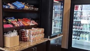 A snack bar with shelves stocked with various snacks and a refrigerator with beverages.