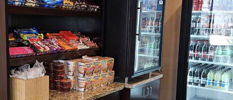 A snack bar with shelves stocked with various snacks and a refrigerator with beverages.