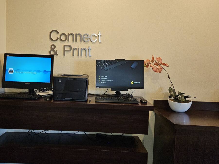 Tauleller de recepció amb dos monitors, una impressora i un cartell que diu "Connect & Print".