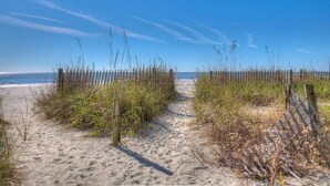 A sandy beach path with wooden fencing and vegetation.