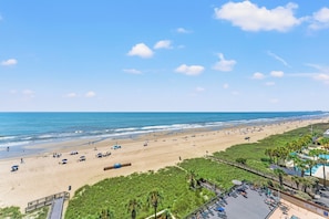 Vista de la playa con un paseo marítimo, sombrillas y una zona de piscina.