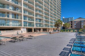 Un hôtel à plusieurs étages doté de balcons, d’un espace piscine avec des chaises longues et d’un ciel d’un bleu éclatant.