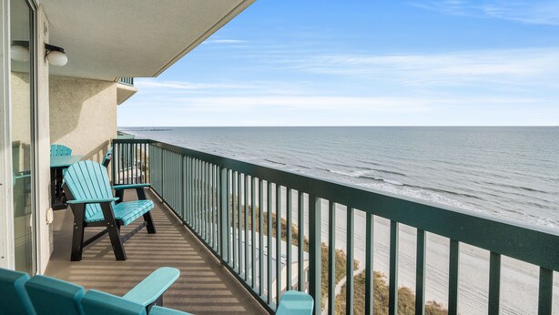 A balcony with two chairs and a table, overlooking the ocean.