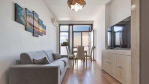 A modern living room with a grey sofa, a dining area with a table and chairs, and a kitchen with cabinets and a TV. - B&B Joy Home - Camera 3 (Maruggio)