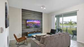 Un salon moderne doté d’un grand téléviseur à écran plat, d’un canapé gris, d’une table basse et d’un coin repas.