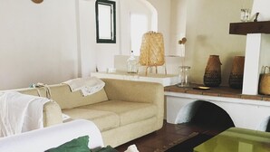 Un salon avec un canapé, une table basse et un pouf vert. On y trouve également une chaise en osier et une lampe posée sur une table.