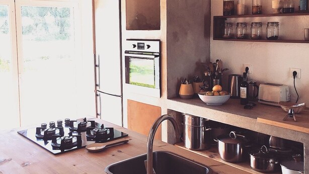 Une cuisine équipée d’une cuisinière à gaz, d’un four et de divers ustensiles de cuisine et bocaux rangés sur des étagères.