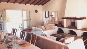Un salon chaleureux avec un plafond en bois, un coin repas avec une table dressée pour quatre personnes et une cheminée.