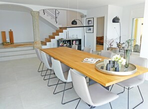 Un espace repas moderne avec une table en bois, des chaises blanches et un îlot central sur lequel est posé un plateau.