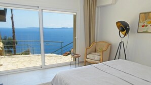 A bedroom with a large bed, a chair, a floor lamp, and a view of the sea through a sliding door. - Villa Bianca, luxury overlooking Canyelles petites beach. Heated pool (Roses)