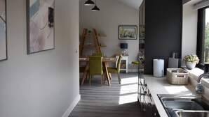 A modern kitchen with a dining area, featuring a wooden table, chairs, pendant lights, and artwork on the walls.