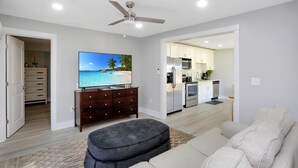 Ein modernes Wohnzimmer mit einem Flachbildfernseher, einem dunklen Hocker und einem hellen Sofa.