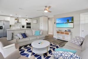 A modern living room with a sofa, coffee table, and a TV displaying a beach scene. - Anchored Inn 3 (Port St. Joe)