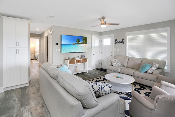 A living room with a large sofa, a coffee table, and a television displaying a beach scene.