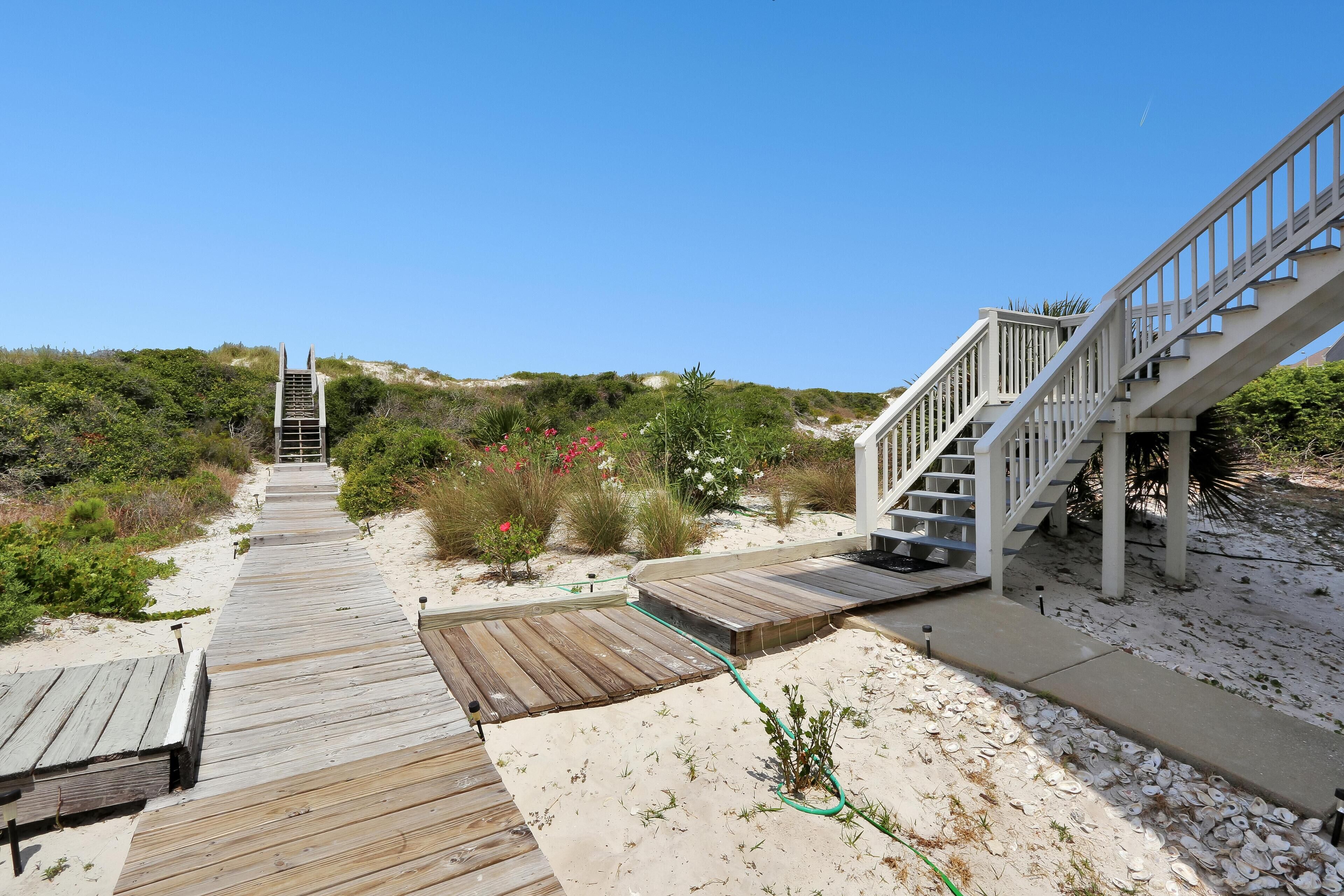 A wooden boardwalk leading to a staircase with a view of a beach and dunes.