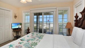 A bedroom with a bed, a television, and a view of the ocean through the sliding glass doors. - A Tropical Breeze (Port St. Joe)