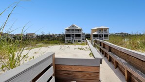 A wooden boardwalk leading to beachfront properties with balconies and a clear blue sky. - A Tropical Breeze (Port St. Joe)