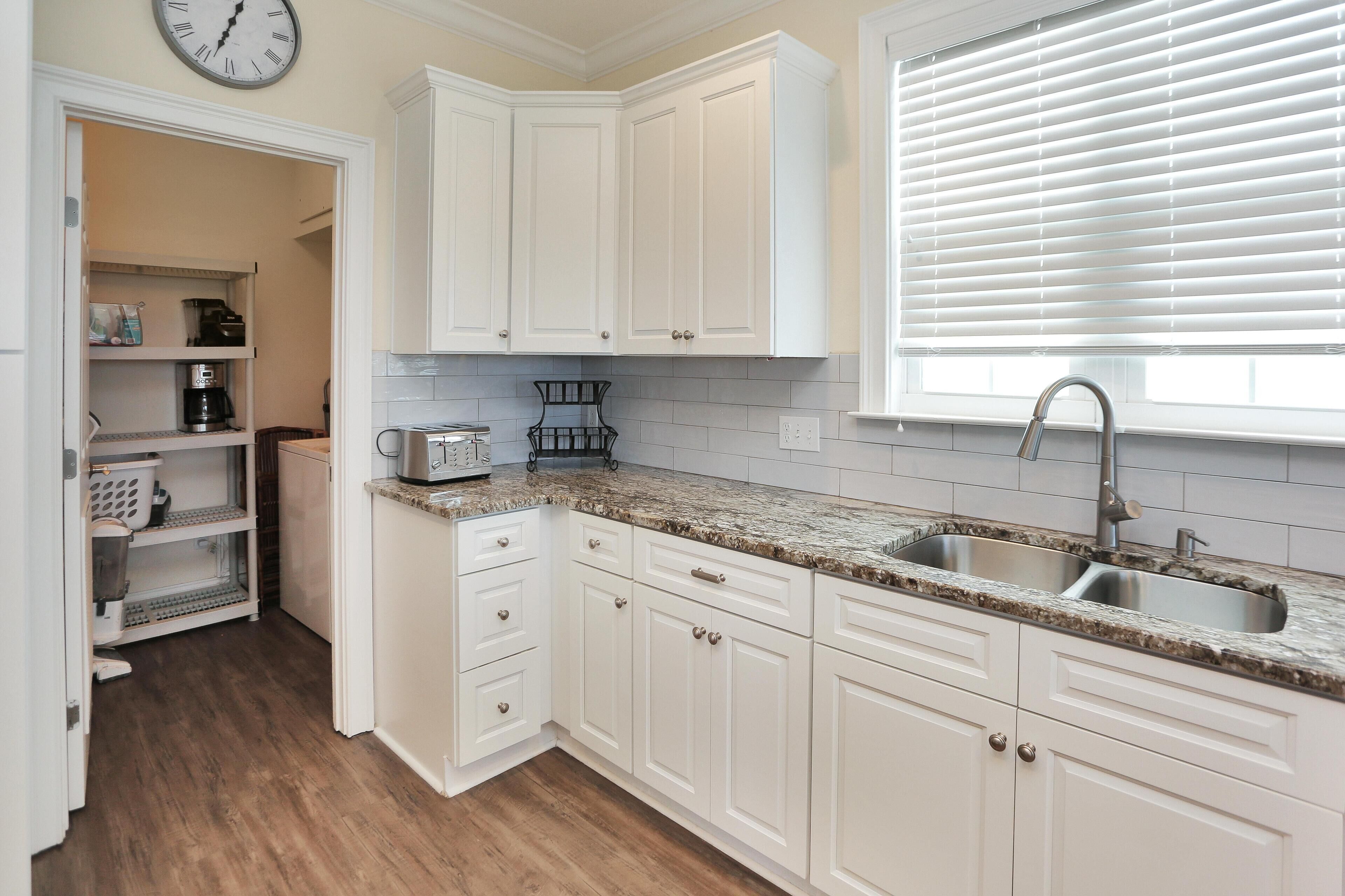 A kitchen with white cabinets, granite countertops, a double sink, and a clock on the wall.