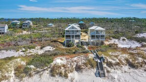 A coastal property with multiple buildings, including a prominent two-story structure with a balcony, surrounded by natural vegetation and sandy terrain. - A Tropical Breeze (Port St. Joe)