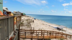 Une vue sur la plage avec une terrasse en bois, des chaises de plage, des parasols et une plage de sable.