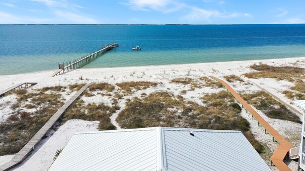A beach view with a wooden pier extending into the ocean, a boat near the pier, and a sandy beach with pathways. - Amethyst Cove (Port St. Joe)