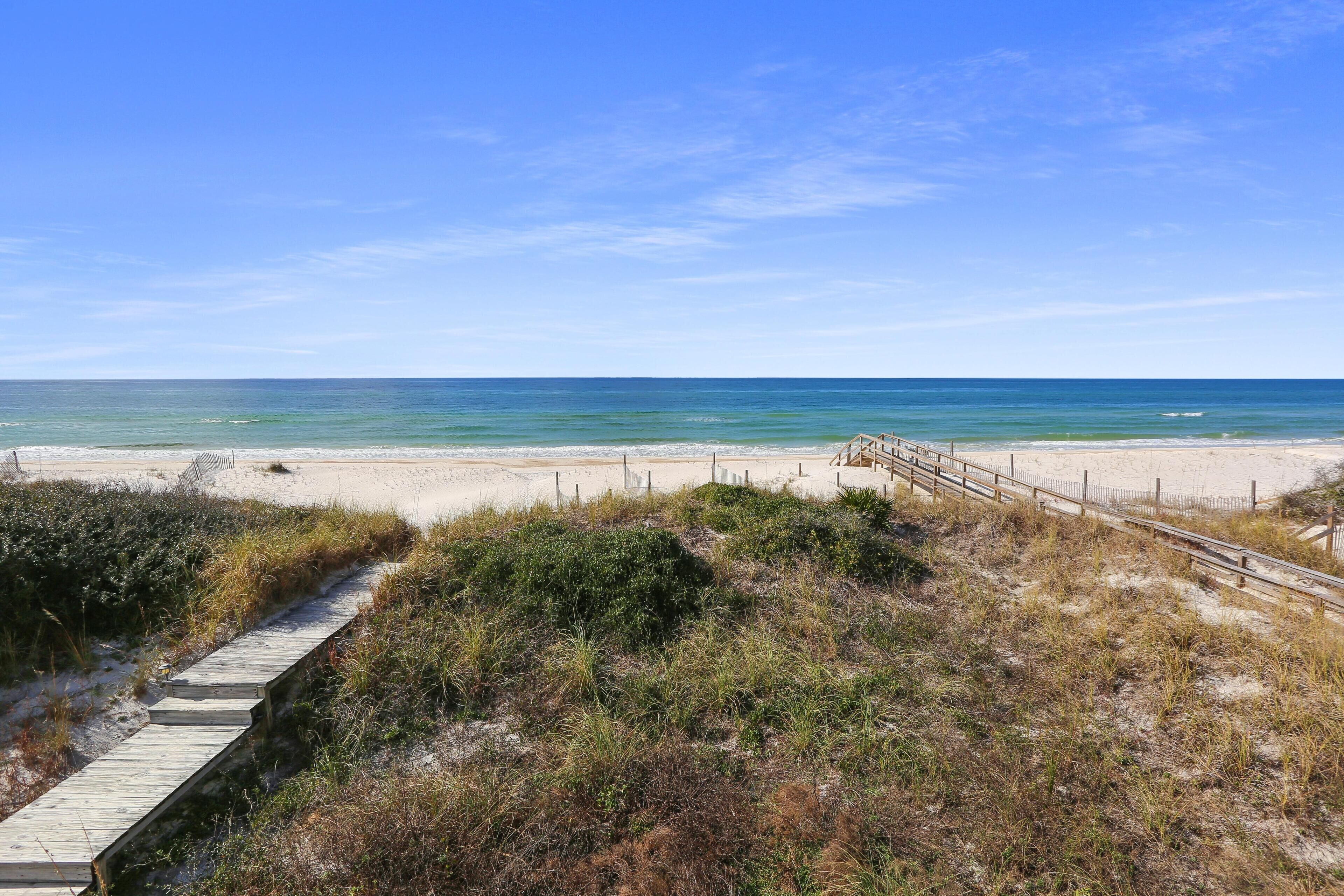 Une plage avec une promenade en bois menant au rivage, une plage de sable et l’océan.