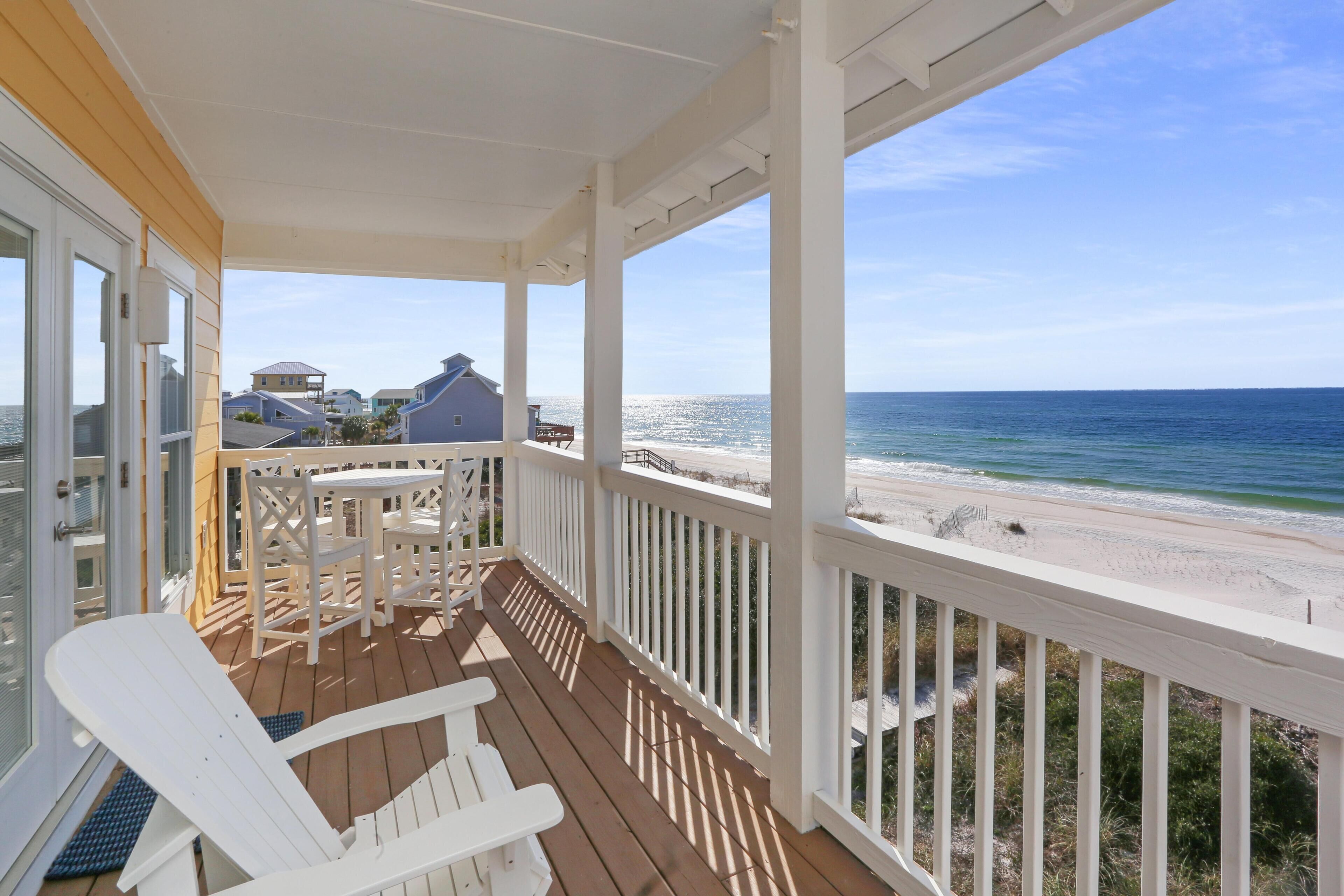 A wooden deck with white railings overlooking a beach.