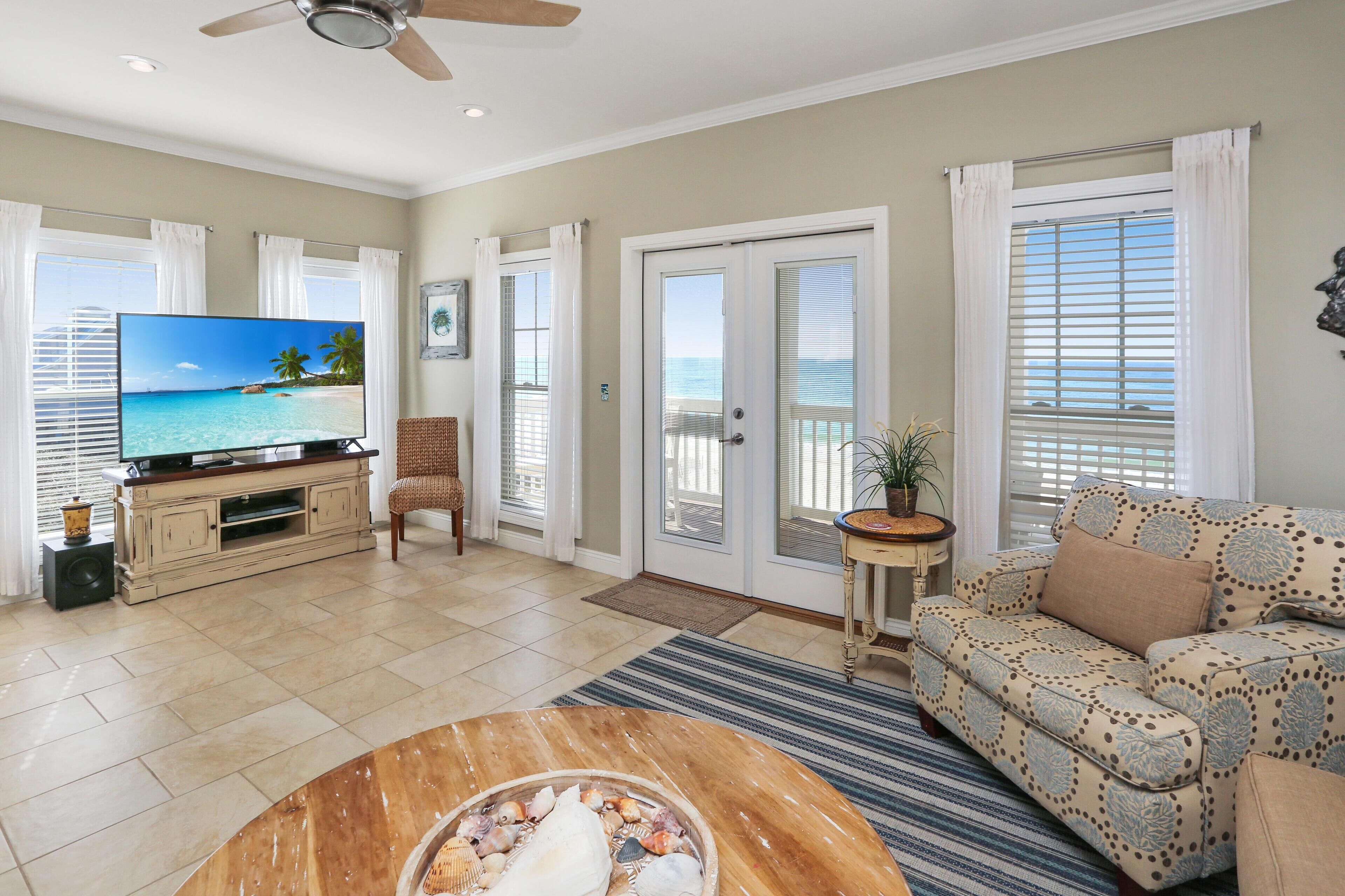 A living room with a television, a sofa, a coffee table, and a view of the ocean through the sliding glass door.
