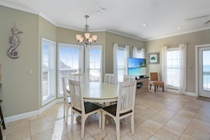 A dining area with a round table and white chairs, a chandelier, and a television on a stand.