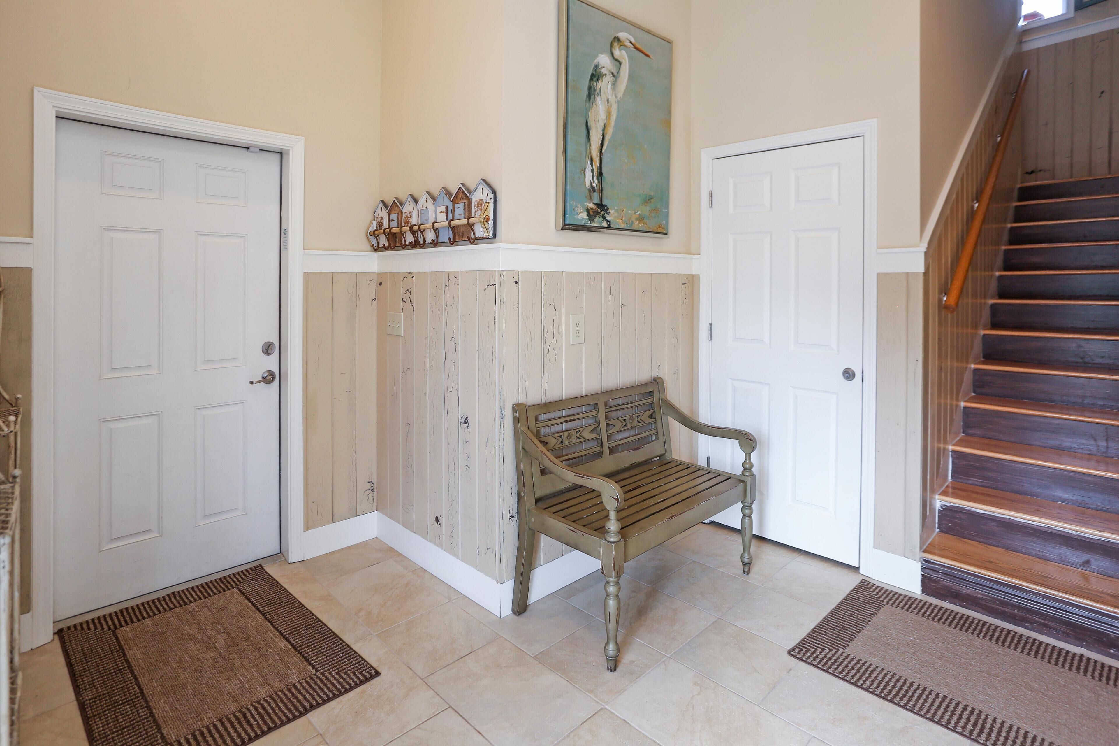 Un couloir avec un banc en bois, deux portes blanches, un escalier en bois et une horloge fixée au mur.