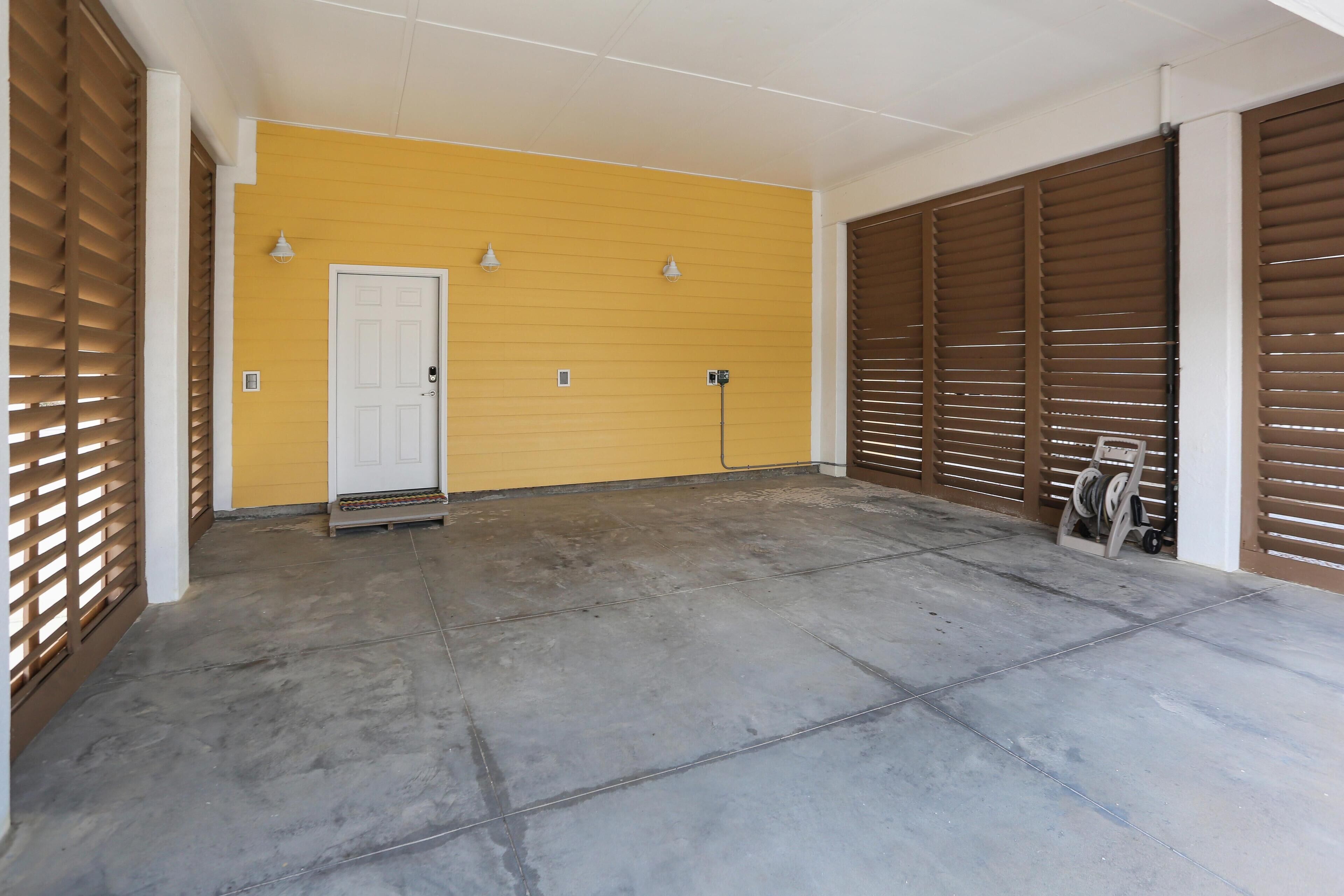 Een ruime garage met een gele muur, een witte deur en bruine luiken.