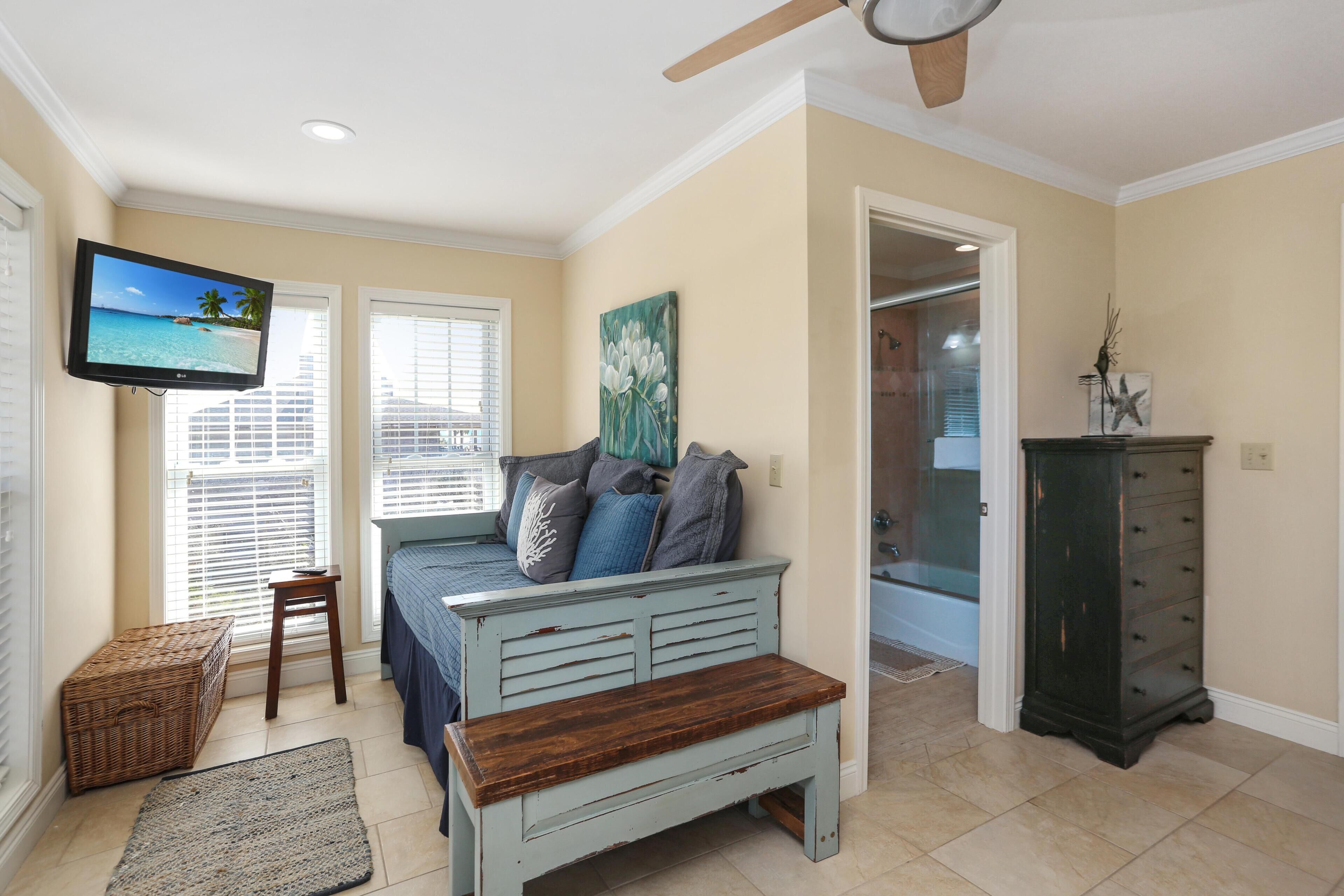 A bedroom with a bed, a television, a bench, a dresser, and a painting.