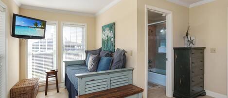A bedroom with a bed, a television, a bench, a dresser, and a painting.