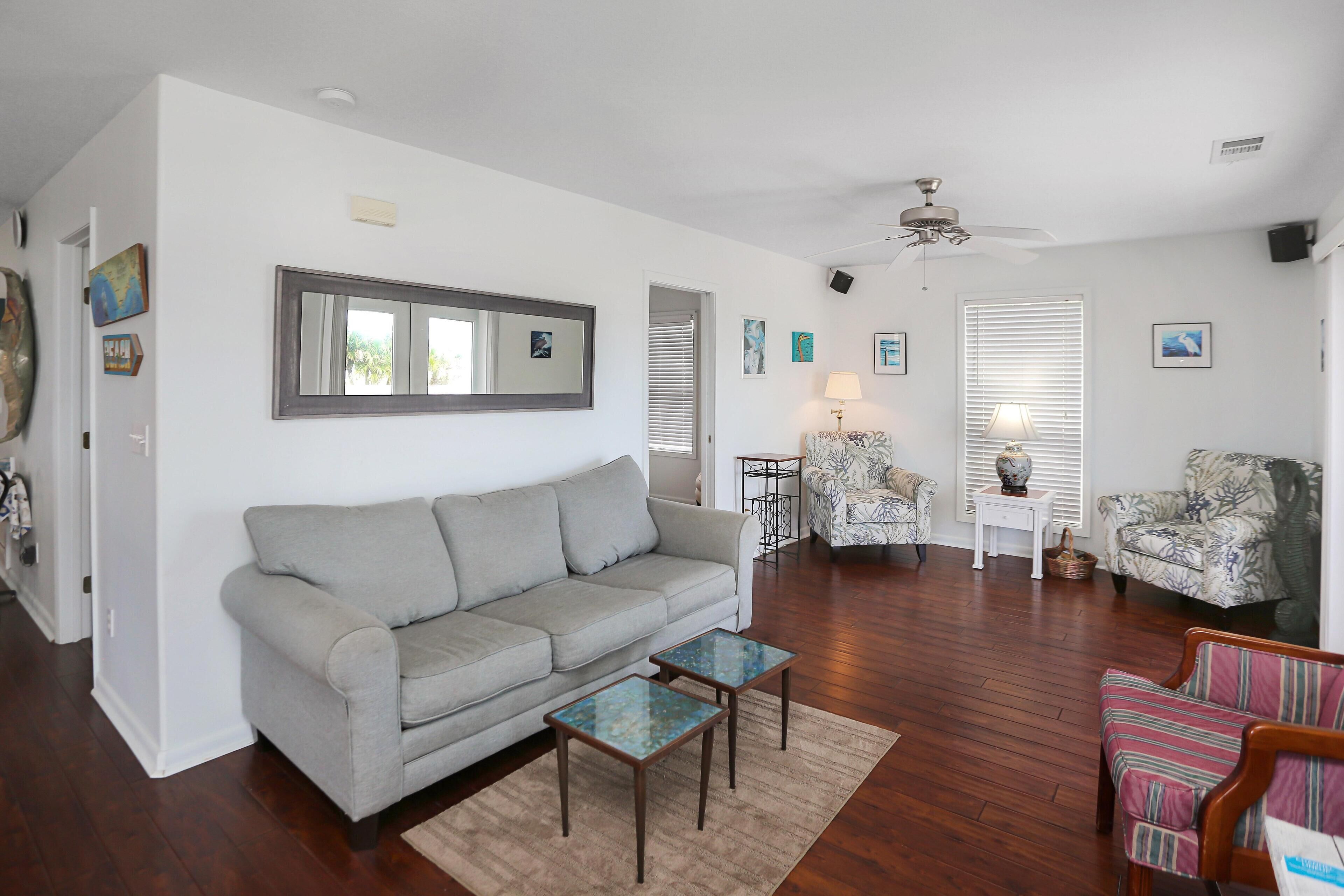 A living room with a grey sofa, two small tables, patterned armchairs, and a ceiling fan.