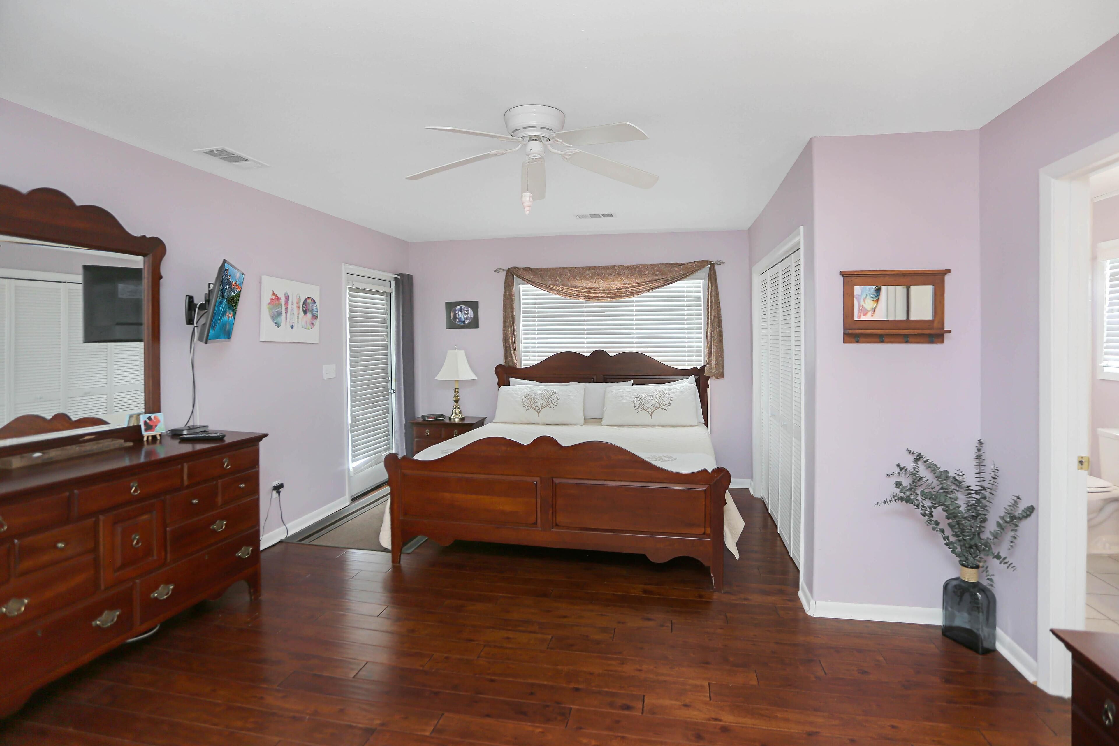 Un dormitorio con cama de madera, cómoda, ventilador de techo y ventana con persianas.