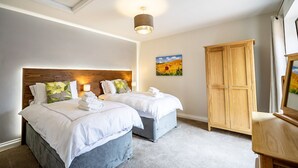 A hotel room with two beds, a wooden wardrobe, a painting on the wall, and a ceiling light fixture. - A family break that sleeps 4 guests  in 2 bedrooms (York)