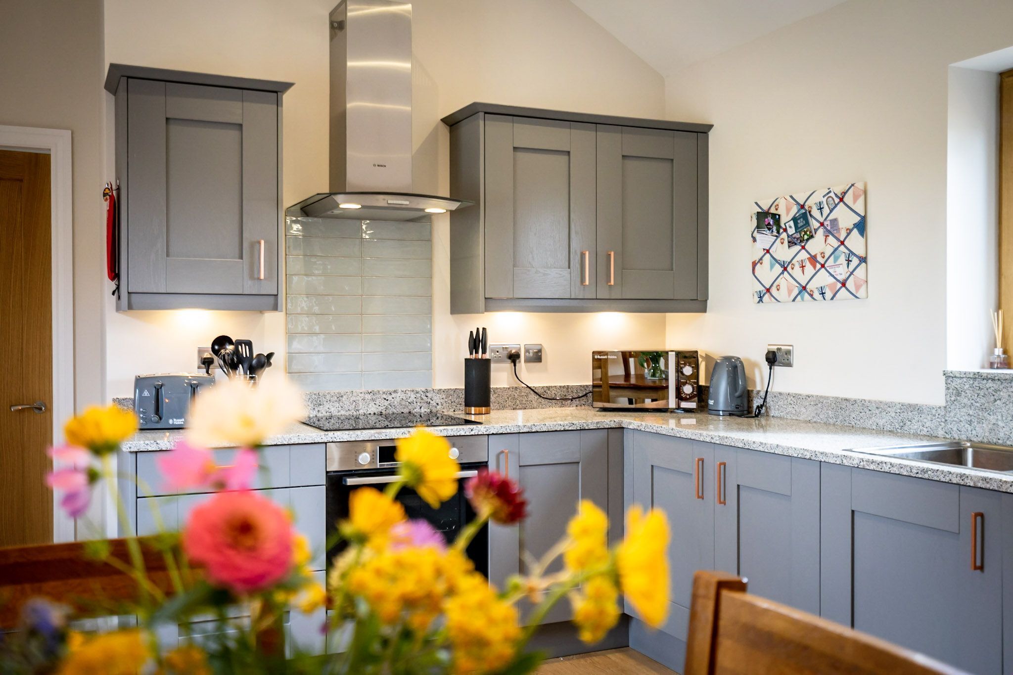 A modern kitchen with grey cabinets, a built-in stove, and a coffee maker.