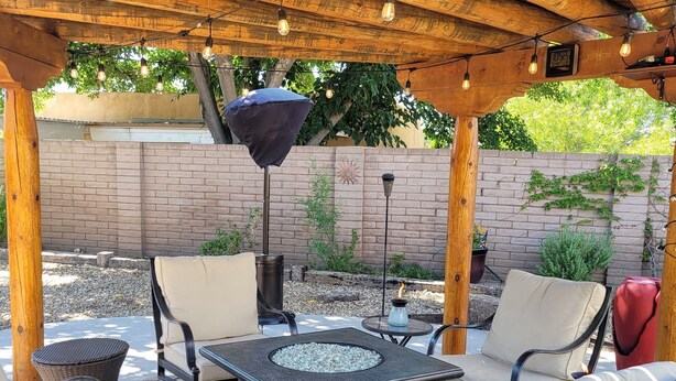 An outdoor patio with a fire pit table, cushioned chairs, and string lights. - Charming, convenient and comfortable!! (Albuquerque)