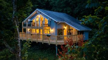 Eine zweistöckige Holzhütte mit Balkon, umgeben von dichtem Wald.