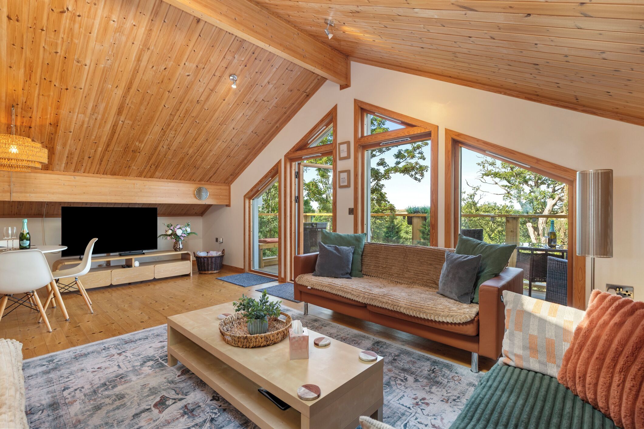 Ein geräumiges Wohnzimmer mit hohen Decken, Holzbalken, einer Sofagarnitur, einem Fernseher und einem Essbereich.