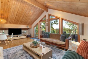 A spacious living room with a high ceiling, wooden beams, a sofa set, a television, and a dining area. - The Rowan - Luxury Lodge and Woodland Views (Penally)